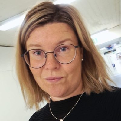 Portrait of Lotta Vuokila. Lotta has blonde hair, glasses and a black shirt.