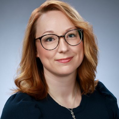 Portrait of Meri-Maija Ollila. Meri-Maija has light brown hair, glasses and kind smile.