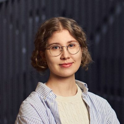 Portrait of Milena Myllykangas. Milena has a light brown hair to the shoulder and glasses. Milena is wearing a light blue blouse.
